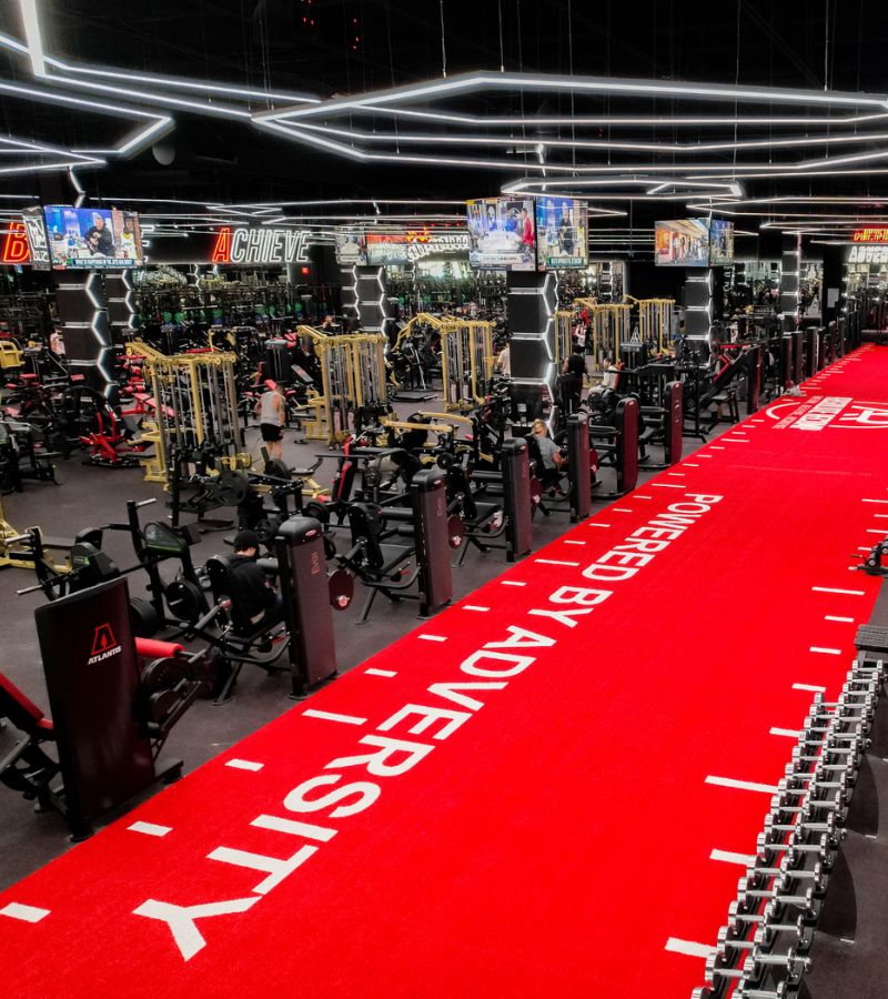 Strength training area at Absolute Recomp Fort Worth with red turf, free weights, and advanced gym equipment.