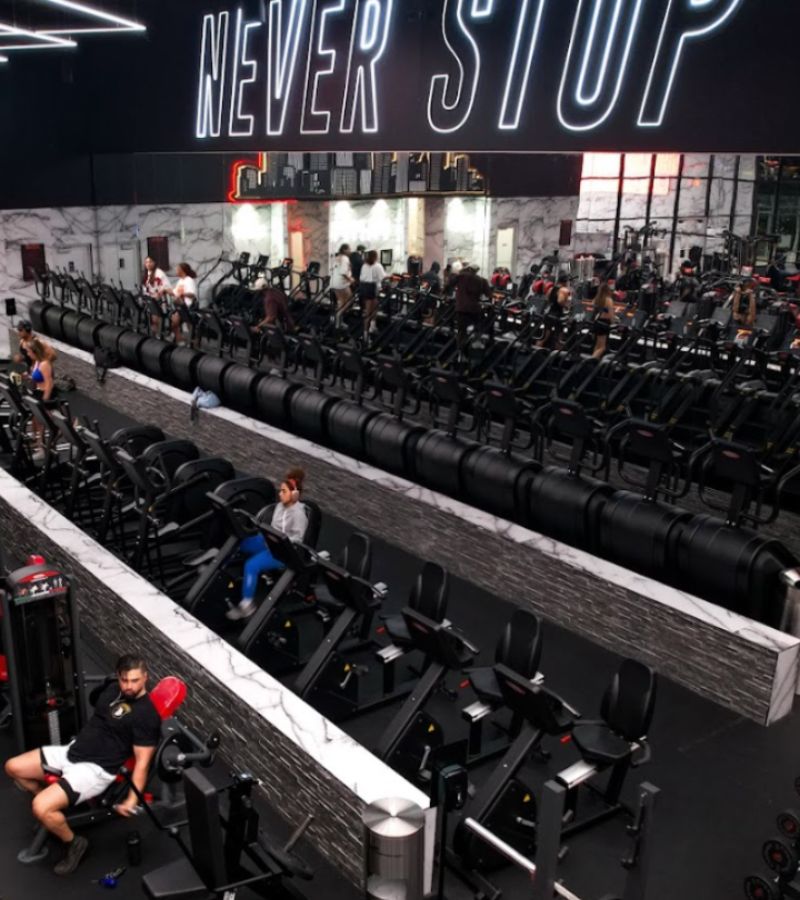 Cardio area at Absolute Recomp Las Colinas featuring treadmills and bikes with bold “Never Stop” gym design.