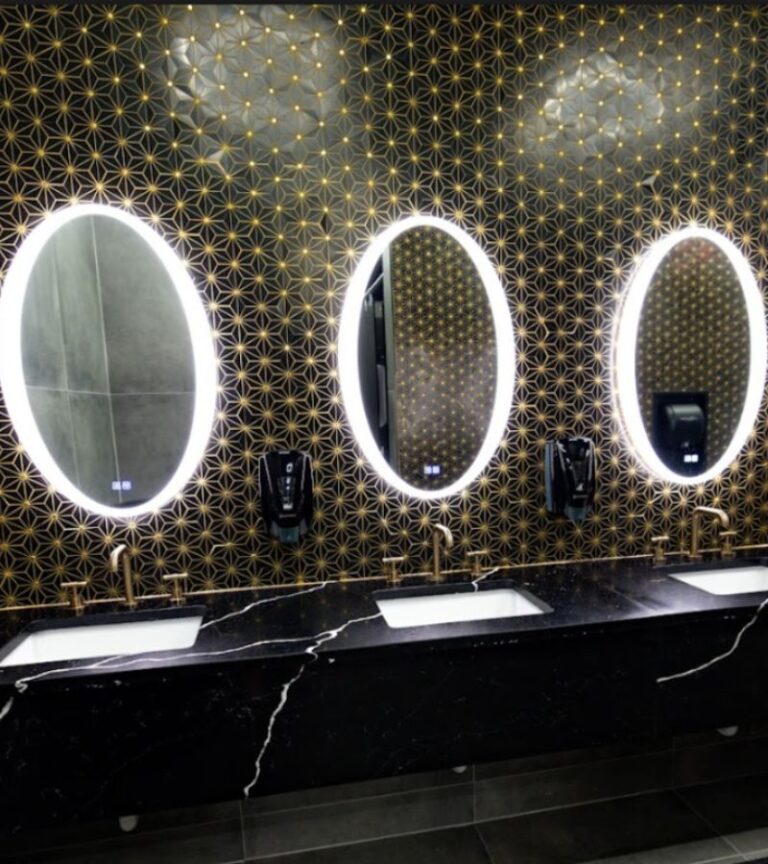 Luxurious locker room vanity with illuminated mirrors and modern black marble sinks at Absolute Recomp Las Colinas.