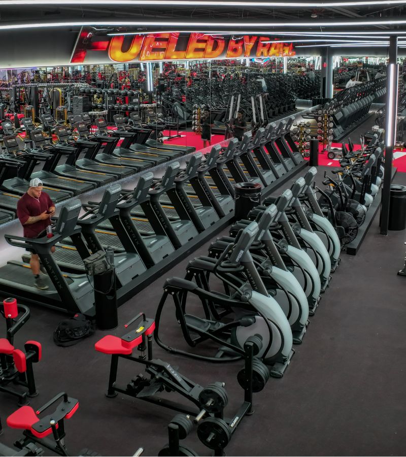 Cardio training area at Absolute Recomp Lewisville featuring treadmills, bikes, and high-end gym equipment in a bold red and black design.