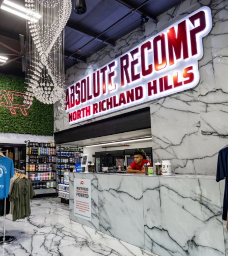 Front desk and retail area at Absolute Recomp North Richland Hills featuring supplements, apparel, and branded gear.